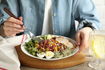 Woman eating delicious salad with brown rice at wooden table, closeup