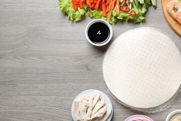 Rice paper sheets and different ingredients on grey wooden table, flat lay. Space for text