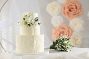 Delicious wedding cake with floral decor and bouquet on table indoors