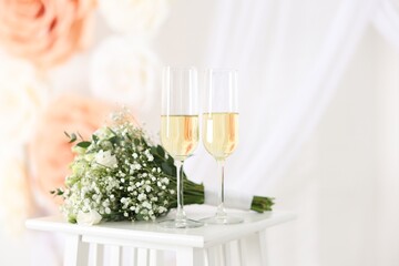 Glasses of champagne and wedding bouquet on table indoors