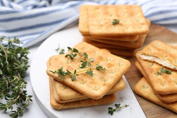 Tasty salty crackers with thyme on white table, closeup