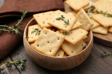 Tasty salty crackers with thyme on wooden table, closeup
