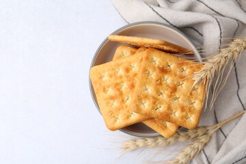 Tasty salty crackers with wheat spikes on white table, top view. Space for text