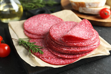 Slices of tasty smoked sausage and rosemary on black table, closeup