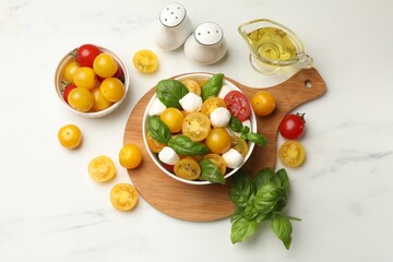 Fresh salad with yellow tomatoes, basil and mozzarella cheese on white marble table, flat lay