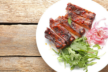 Delicious spare ribs, onion and arugula on wooden table, top view. Space for text