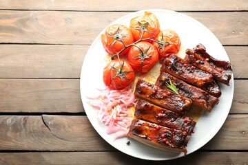 Delicious spare ribs, onion and sun dried tomatoes on wooden table, top view. Space for text