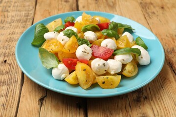 Tasty salad with yellow tomatoes, basil and mozzarella cheese on wooden table, closeup