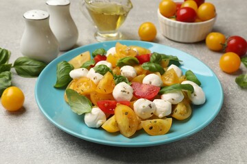 Tasty salad with yellow tomatoes, basil and mozzarella cheese on light grey table, closeup