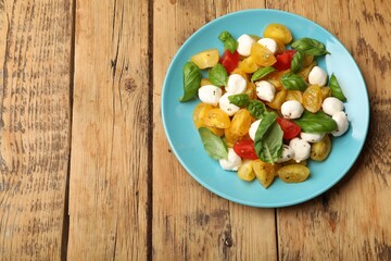 Tasty salad with yellow tomatoes, basil and mozzarella cheese on wooden table, top view. Space for text