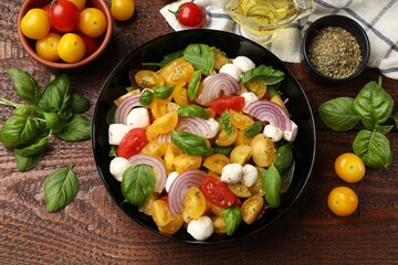 Tasty salad with yellow tomatoes, basil, onion and mozzarella cheese on wooden table, flat lay