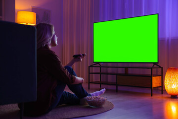 Woman watching TV set with green screen at home in evening. Chroma key compositing