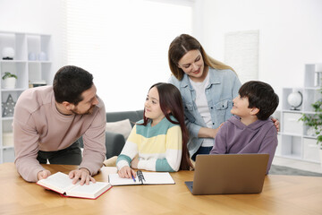 Parents helping their kids with homework at wooden table indoors