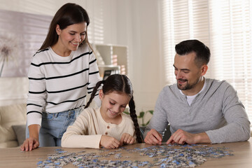 Fototapeta premium Happy parents and their daughter solving puzzle together at wooden table indoors