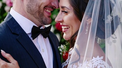 Groom and bride, standing close together, exchange loving glances and laughter, creating a heartwarming scene of marital bliss amidst a backdrop of vibrant flowers