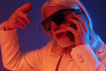 Stylish elderly man in sunglasses talking on the phone with an expressive pose, set against a...