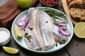 Marinated herring fillets with onion rings, rosemary, lime and spices on wooden table, closeup