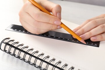 Woman drawing sketch with ruler and pencil on notebook at light table, closeup