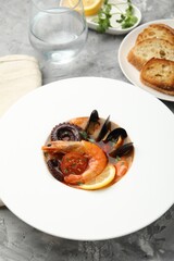 Delicious seafood soup in bowl, pieces of bread and water on gray textured table, closeup