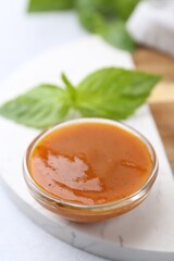Tasty curry sauce in glass bowl and basil on white table, closeup