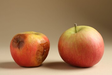 Rotten and fresh apples on beige background, closeup