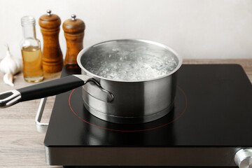 Saucepan with boiling water and stove on wooden table against white background, closeup
