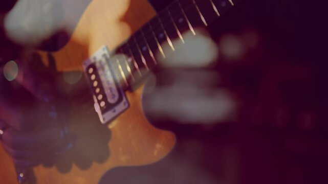 Gloved hand playing electric guitar under moody colored stage lighting, showing soft bokeh circles