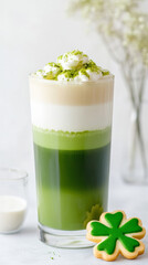 Matcha latte with cream layer and shamrock cookie in tall glass for st. patrick's day celebration