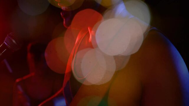 Male singer wearing headphones singing into microphone in music studio with animated bokeh lights