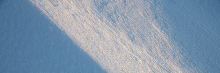 Beautiful winter background with snowy ground. Natural snow texture. Wind sculpted patterns on snow surface. Wide panoramic texture for background and design. Closeup top view with copy space.
