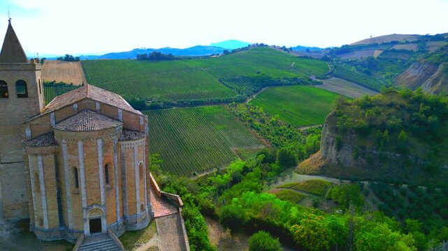 OFFIDA, ITALY - AUGUST 4, 2024: Aerial pan left shot of Chiesa di Santa Maria della Rocca. Perched on cliffs, Santa Maria della Rocca overlooks verdant, sweeping valleys, lush greenery, promontories