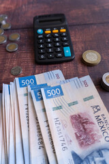 Several $500 Mexican peso bills and coins around a calculator on a table