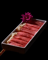 A tray of meat is displayed with a purple flower in the background