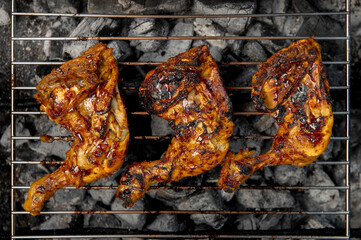 Three pieces of chicken are on a grill, with one piece being the largest