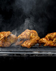 Three pieces of chicken are on a grill, with smoke coming from them