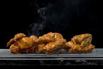 Three pieces of chicken are on a grill, with smoke coming from the grill
