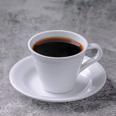 A white coffee cup with a black liquid in it sits on a white plate