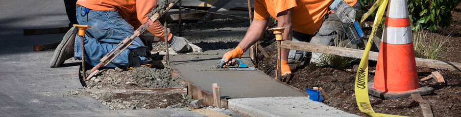 Work crew pouring fresh cement for a low and wide curb, workmen smoothing concrete with hand...