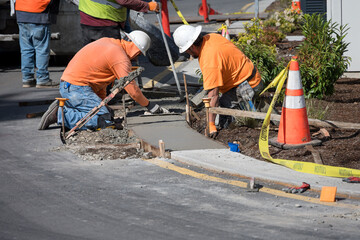 Work crew pouring fresh cement for a low and wide curb, workmen smoothing concrete with hand...