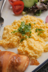 Delicious scrambled eggs served with salad and croissant for breakfast