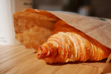 Croissant in a paper bag on a wooden table in a cozy cafe setting