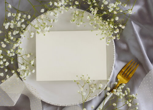 Greeting card mockup, menu blank mock up, wedding card, wedding invitation on table place setting ,white flowers frame on grey silk background top view. Space for text.Holiday backdrop