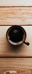 Fototapeta premium A top-down view of a black coffee cup resting on a wooden surface, highlighting a warm, cozy atmosphere.