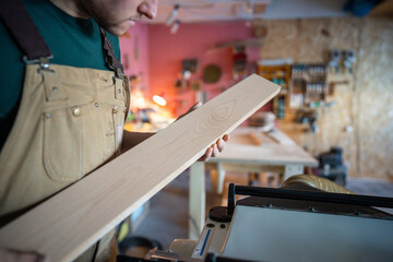 Unrecognizable joiner examining wooden board for quality before processing in workshop. Woodworking...