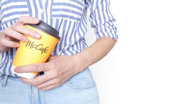 Woman holding a yellow McCafe coffee cup wearing blue jeans and blue striped shirt. Ottawa ON Canada 06-17-2024