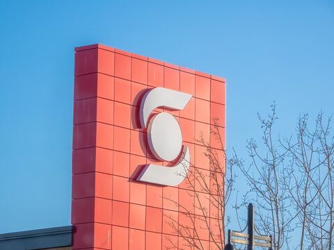 Calgary, Alberta, Canada. Apr 25, 2025. A large, stylized "S" logo, the emblem of Scotiabank, prominently displayed in white against a textured red building facade under a clear blue sky.