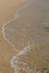 White foam from ocean waves washes onto the sandy beach shore under the summer sun, creating a beautiful seascape