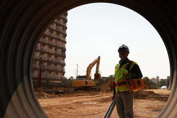 A Male Project engineer holds drawing work inside a huge pipe of an infrastructure project