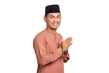 Smiling young Asian Muslim man gesturing Eid Mubarak greeting isolated on transparent background