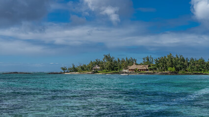 Tropical seascape. Ripples on the surface of the turquoise ocean. On the shore, among the green trees, you can see the hotel building. The boat is anchored. Blue sky, clouds. Mauritius. Belle Mare.